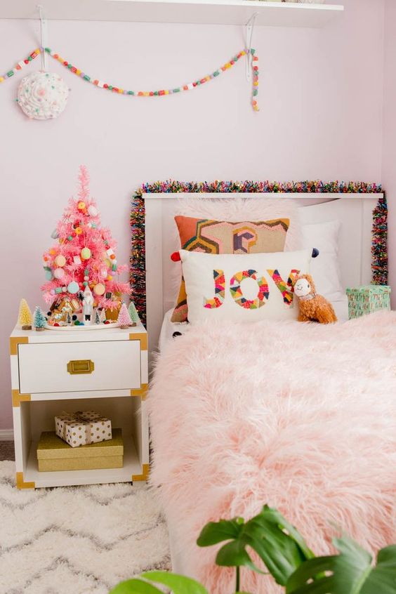 A-tiny-pink-christmas-tree-with-colorful-ornaments-a-bright-pompom-garland-and-a-printed-pillow-for-holiday