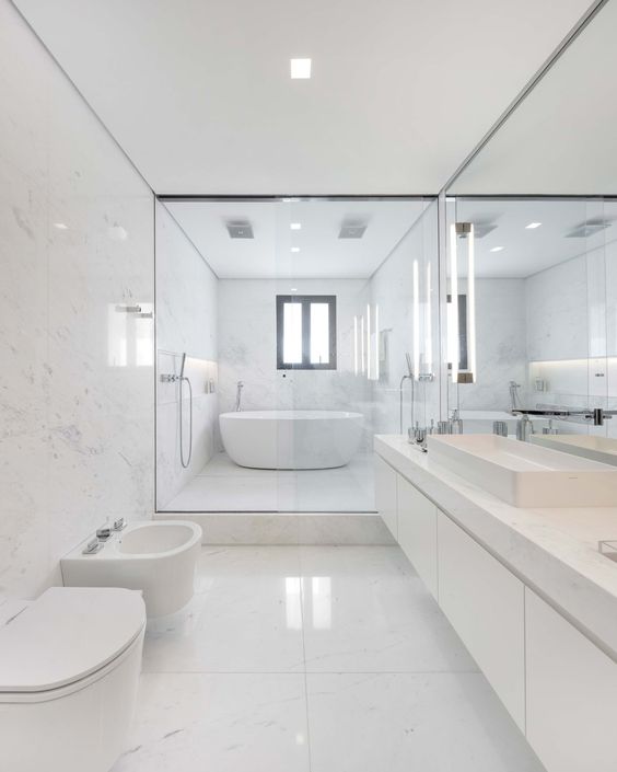 A-chic-minimalist-bathroom-clad-with-large-scale-white-marble-tiles-a-floating-marble-vanity-and-white-appliances