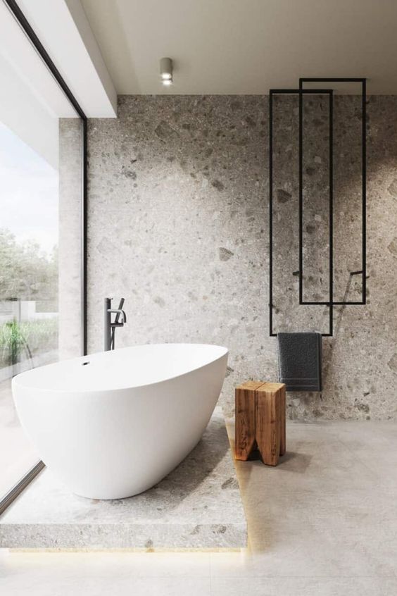 A-minimalist-bathroom-with-a-glass-wall-a-bathtub-on-a-stone-platform-a-stone-wall-and-cool-towel-hangers